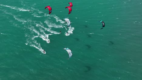Wide-aerial-shot-of-a-group-of-kitesurfers-racing-across-the-ocean-in-the-high-wind-on-light-green-sea,-Northern-Brazil