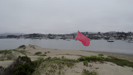 Aerial-Circle-Dolly-Around-Red-Flag-Fluttering-On-Beach-Near-Morro-Bay