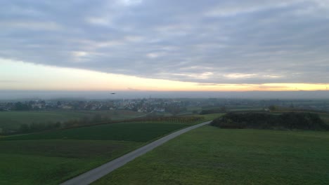 Drone-Camera-Hovering-Over-Green-Meadows-Near-Idyllic-Village