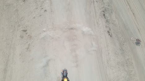 aerial-footage-of-a-motorcyclist-spinning-in-a-circle-on-a-dirt-road,-kicking-up-the-dust