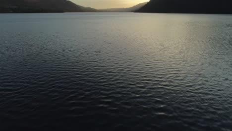 Slow-Low-Aerial-Drone-Shot-Panning-Up-To-Reveal-Stunning-Sunrise-Over-Ullswater-Lake-on-Beautiful-Morning-Lake-District-Cumbria-United-Kingdom