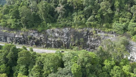 Aerial-shot,-revealing-road-cutting-straight-the-mountain-and-thick-jungle-or-forest