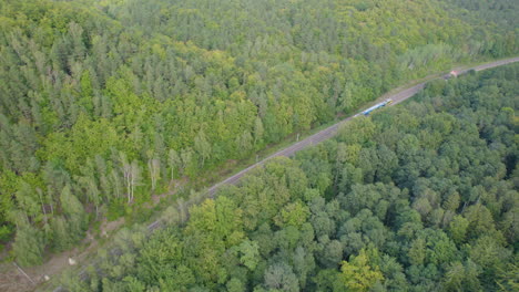 Aerial-tracking-shot-train-on-rails-surrounded-by-forest-trees-in-sunset---Gdynia-City-in-background,-Poland