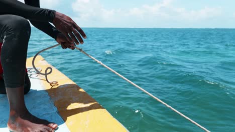 Ein-Schwarzer-Fischer,-Der-Das-Seil-Vom-Anker-Seines-Bootes-Hält,-Das-Auf-Dem-Tiefblauen-Ozean-Schwimmt