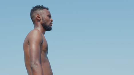 a-black-man-with-a-beard-in-bare-torso-looking-around-against-a-bright-blue-sky