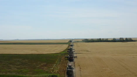 Aerial-follow-shot-behind-combine-harvesters-in-Saskatchewan,-Canada-farmland