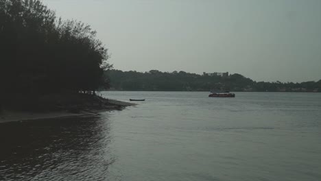 A-stationary-boat-off-the-bank-of-the-Mandovi-River-surrounded-by-the-beautiful-natural-landscape-along-the-riverbank,-Panjim,-India