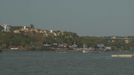 A-beautiful-morning-along-the-Mandovi-River-as-a-commercial-fishing-boat-passes-a-ferry-carrying-a-tour-group-on-a-day-trip-heading-out-onto-the-open-water,-Panjim,-India