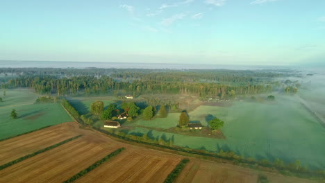 Aerial-drone-forward-moving-shot-over-agricultural-farmlands-beside-village-houses-on-an-early-morning-along-rural-countryside