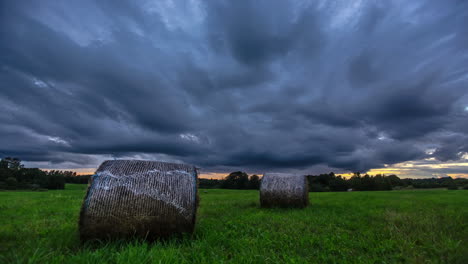 Stormy-Clouds-Rolling-Over-Agricultural-Land-With-Hay-Rolls-In-Meadows