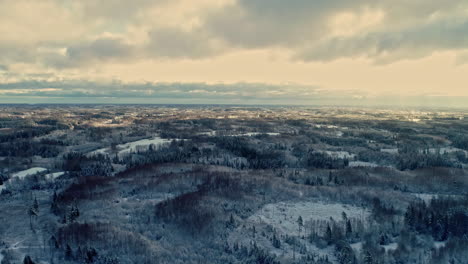 Aerial-drone-shot-of-winter-landscape-with-snow-covered-forest-in-cold-highlands-along-rural-countryside-on-a-cloudy-day