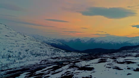 Aerial-drone-panning-shot-over-snowed-road-in-mountains-with-colorful-sky-at-sunrise
