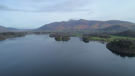 Aerial-Drone-Shot-Backwards-Over-Derwentwater-Lake-Keswick-Moving-Away-From-Skiddaw-Mountain-in-Background-on-Sunny-Morning-with-Clouds-Lake-District-Cumbria-United-Kingdom