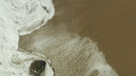 Aufsteigende-Luftaufnahme-Von-Schäumenden-Wellen,-Die-über-Den-Sandstrand-Rauschen