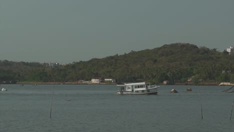 A-view-from-the-bank-of-the-Mandovi-River-as-a-commercial-fishing-boat-travels-downstream-heading-out-for-day-of-fishing,-Panjim,-India