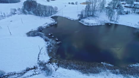 Aerial-drone-forward-moving-shot-over-a-beautiful-winter-frozen-lake-along-cold-winter-landscape-on-a-cloudy-day