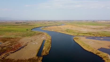 Aerial-establishing-shot-over-wide-river-running-through-fields,-irrigation