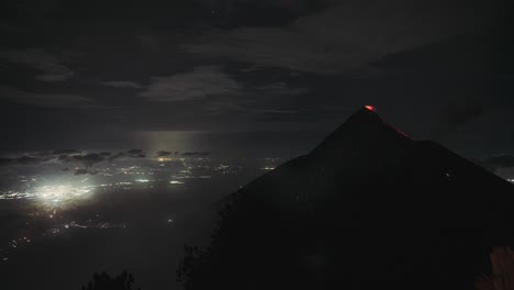 Volcán-De-Fuego-En-Erupción-Por-La-Noche-Con-Lava-Brillante-Y-Luces-De-La-Ciudad-Debajo,-Lapso-De-Tiempo-Nocturno