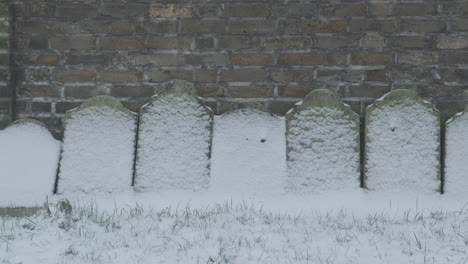 Anonyme-Schneebedeckte-Grabsteine-Gegen-Rote-Backsteinmauer-An-Einem-Wintertag-Auf-Einem-Friedhof
