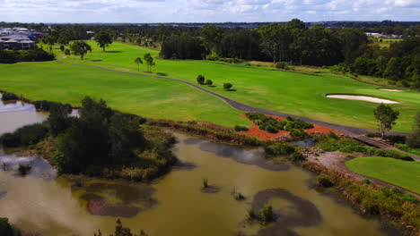 Golfistas-Jugando-En-La-Calle-Del-Campo-De-Golf-Bajo-Un-Hermoso-Cielo-Azul-Pan-Hasta-El-Lago-Y-La-Comunidad-Suburbana
