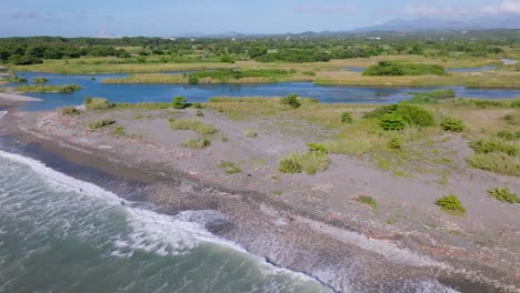 Aerial-view-of-River-Mouth-of-Rio-Nizao-surrounded-by-sea,rocky-field-and-green-landscape-in-backdrop