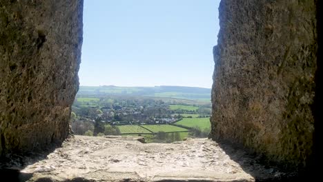 Inside-structural-remains-of-Corfe-castle,-with-the-view-pov-view-through-window-showing-country-side-and-a-small-homestead