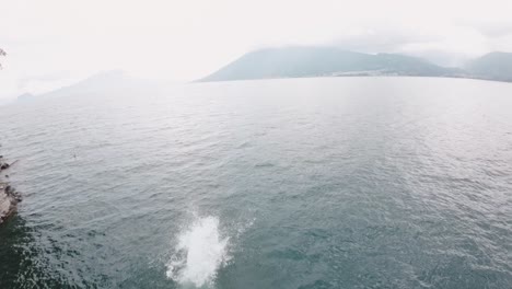 Person-dive-into-lake-Atitlan-on-foggy-day,-aerial-FPV-view