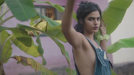 Bold-and-beautiful-south-Asian-woman-looking-through-banana-leaves-wearing-denim-dungarees-with-revealing-upper-body-parts-and-bohemian-look
