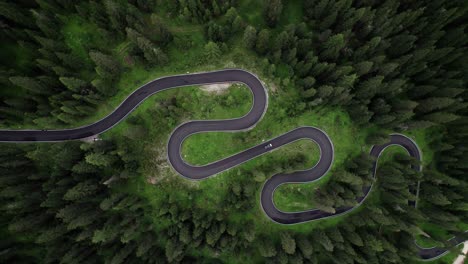 Aerial-top-down-of-car-drive-on-winding-green-forest-curved-road-in-Dolomiti