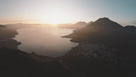 Bright-golden-sunrise-above-silhouette-of-mountains-near-lake-Atitlan,-aerial-view