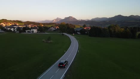 Black-suv-car-drives-towards-mountains-at-sunset-setting-in-Austria