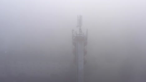 Telecommunication-broadcasting-antennas-in-a-fog-on-water-tower,-aerial-orbital-view