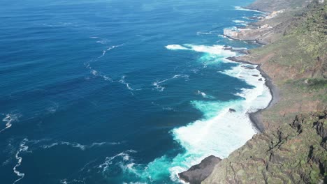 Aerial-view-of-a-giant-cliff-with-the-powerful-waves-of-the-ocean-breaking-on-a-beautiful-sunny-day-in-Tenerife,-Canary-Islands