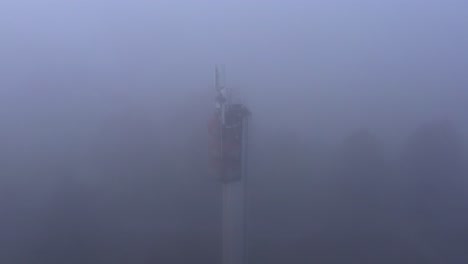 Communication-antennas-on-water-tower-in-thick-fog-with-poor-visibility,-aerial-tilt-down