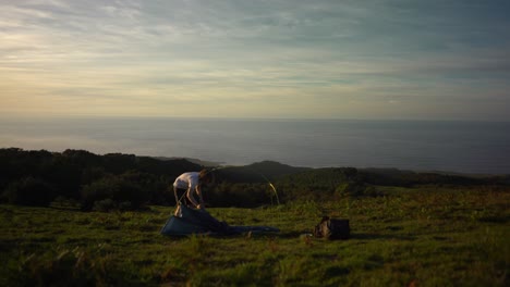 Hiker-pitching-a-tent-with-ocean-view-at-sunset