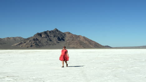 Woman-Walking-and-twirling-in-pink-dress-on-Salt-Flats-near-mountain