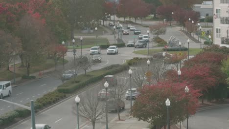 High-angle-of-a-city-intersection,-with-autumn-trees,-streetlights,-and-multiple-cars-passing