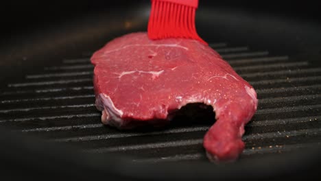 Close-up-slow-motion-shot-of-a-red-kitchen-brush-brushing-a-beef-steak-with-oil-while-frying-in-the-kitchen-for-a-delicious-dinner