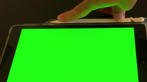 Man-puts-away-pen-after-use-on-ipad-with-green-screen-top-view