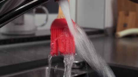 Close-up-handheld-shot-of-cleaning-an-oil-brush-under-running-water-at-the-sink-in-the-kitchen-in-slow-motion