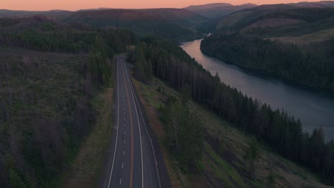 Drone-Shot-of-a-Country-highway-next-to-a-river-during-sunset-with-vehicles-driving