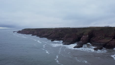 Drone-shot-of-cliffs-in-Northern-Scotland-on-a-grey-day-as-the-waves-crash-over-them