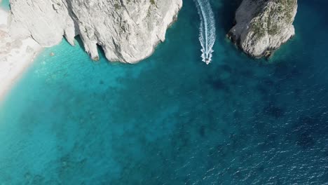 Drone-hovers-above-small-islands-on-the-island-of-Zakynthos,-Greece,-following-a-small-boat-that-emerges-between-two-islands