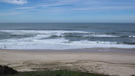 Waves-crashing-on-to-sandy-beach-with-blue-skies-and-horizon-line-visible,-Atlantic-Ocean,-Portugal