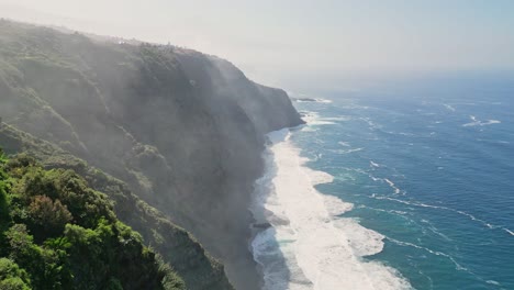 Aerial-view-of-a-giant-cliff-with-the-powerful-waves-of-the-ocean-breaking-on-a-beautiful-sunny-day