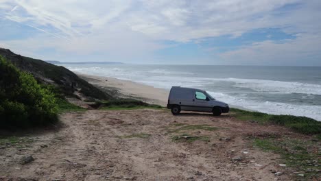 Micro-camper-van-parked-next-to-cliffs-above-sandy-beach-and-Atlantic-Ocean-in-Portugal