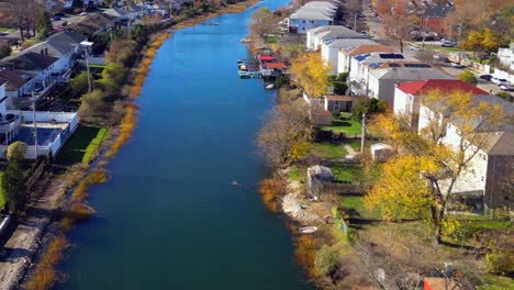 An-aerial-view-along-a-neighborhood-channel,-running-behind-houses-on-a-sunny-day