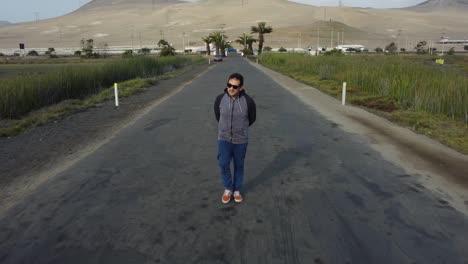 Person-wearing-sunglasses-walking-down-paved-road-with-grassland-on-either-side