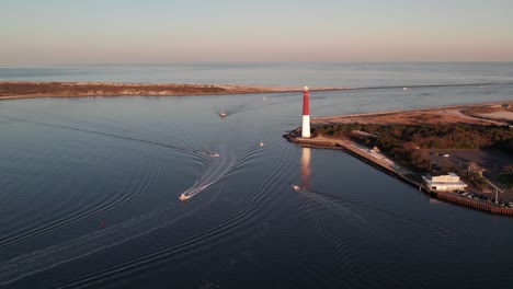 Aerial-drone-view-of-boats-moving-around-Barnegat-Lighthouse-at-sunset