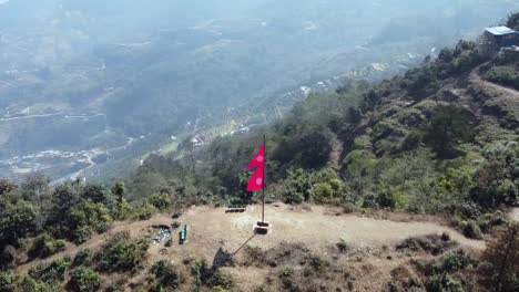 Eine-Spiralförmige-Luftaufnahme-Einer-Nepal-flagge,-Die-Auf-Der-Spitze-Eines-Hügels-In-Den-Ausläufern-Des-Himalaya-In-Nepal-Angebracht-Ist